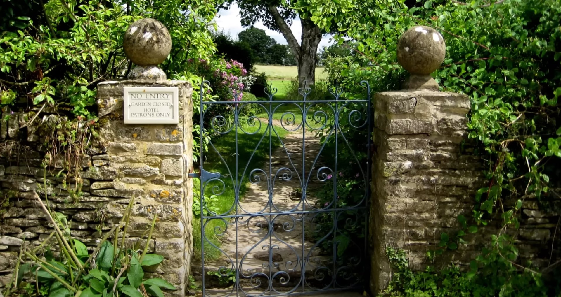 Elegant stone entrance with decorative iron gates and mature landscaping
